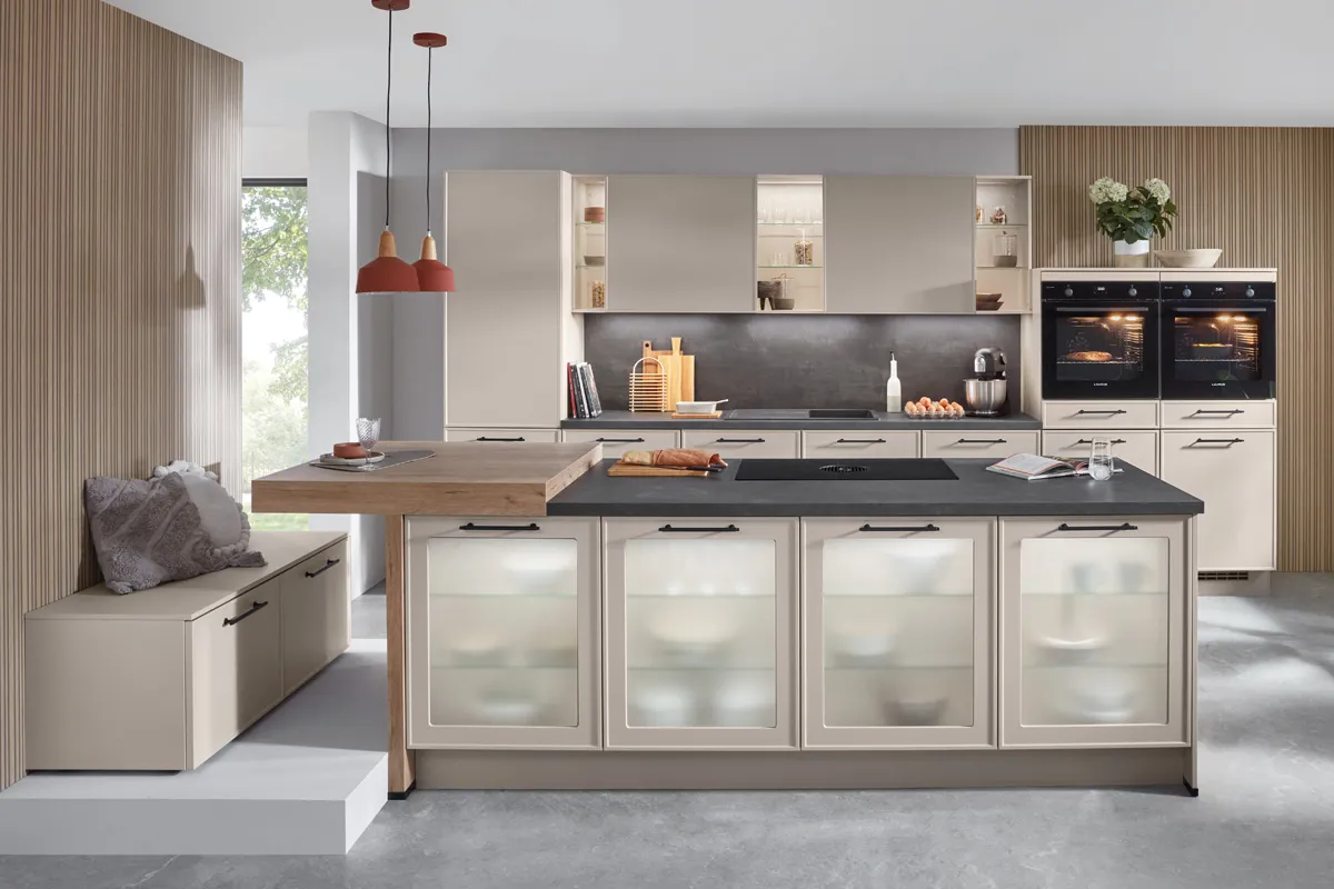 Küche in Sand mit Kochinsel, beleuchteten Glasfronten, zwei Backöfen und angesetzter Sitzbank